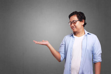 Young Asian man wearing blue and white shirt showing something on empty hand, smiling expression. Close up body portraitの写真素材