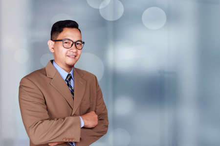 Young Asian businessman wearing suit and glasses smiling looking at a camera, crossed armの写真素材