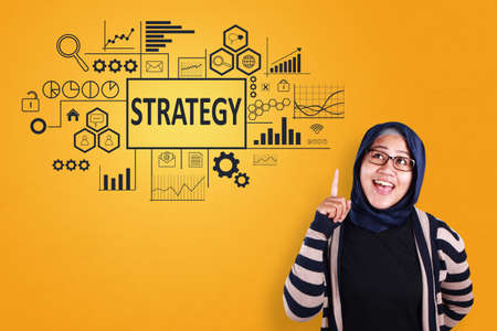 Business Concept. Smiling happy successful asian muslimah entrepreneur with strategy words on virtual screen. Modern Text typography designの写真素材