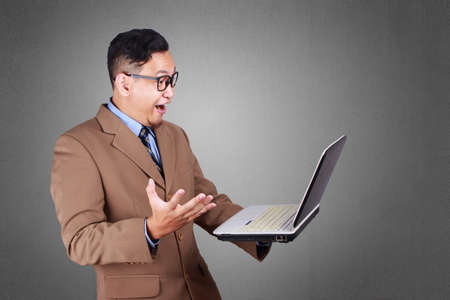 Young Asian businessman looking at laptop, surprised expression. Close up body portrait. Side viewの写真素材