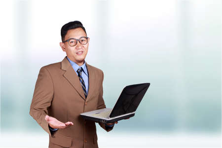 Young Asian businessman wearing suit explaining something, holding laptop. Close up body portrait