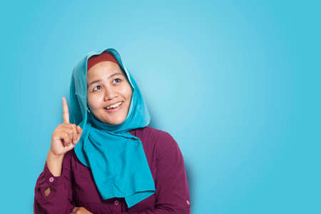 Asian muslim woman wearing blue hijab with thinking expression, copy space. Over blue background. Close up head and shouldersの写真素材