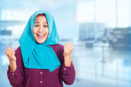 Portrait of success beautiful muslim businesswoman wearing hijab showing winning victory gesturover blurred backgroundの写真素材