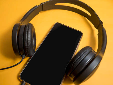 Headphone and smartphone. Earphones on orange background. Listening music sound on mobile phone...