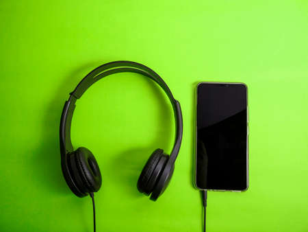 Headphone and smartphone. Earphones on green background. Listening music sound on mobile phone...