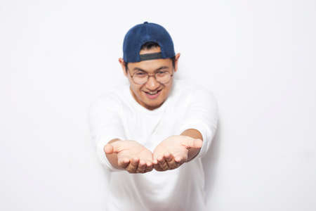 Portrait of happy young Asian man showing something on his empty hands, copy space template over white background, with selective focus areaの写真素材