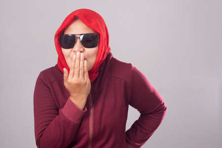 Close up portrait of Asian muslim lady in red suit and hijab laughing smiling mocking at someone while covering her mouth with handの写真素材