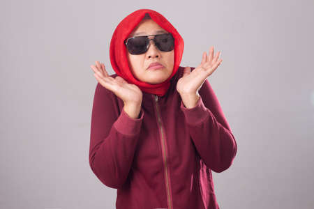 Portrait of Asian muslim lady wearing black sunglasses in red suit and hijab shows refusal or denial gesture, shoulder shrug, I don't know expressionの写真素材