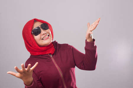 Portrait of Asian muslim lady wearing black sunglasses in red suit and hijab shows refusal or denial gesture, shoulder shrug, I don't know expressionの写真素材