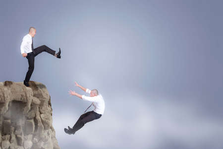 Bad business competition concept. Businessman kicking down his competior over the cliffの写真素材