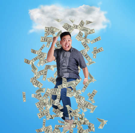 Portrait of happy successful young Asian billionaire man smiling happily under rain of money. Wealth...