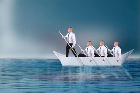 Leader businessman ;ead his team paddling on boat of paper in the ocean, teamwork challenge in...