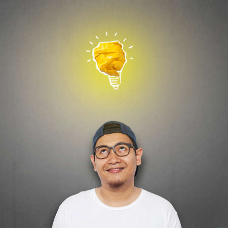 Portrait of successful handsome Asian man smiling happy with bright light bulb lamp made of paper, symbol of idea and innovationの写真素材