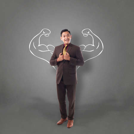 Business power concept. Young  Asian businessman  smiling with strong powerful arms drawn behind. Inner power authorityの写真素材