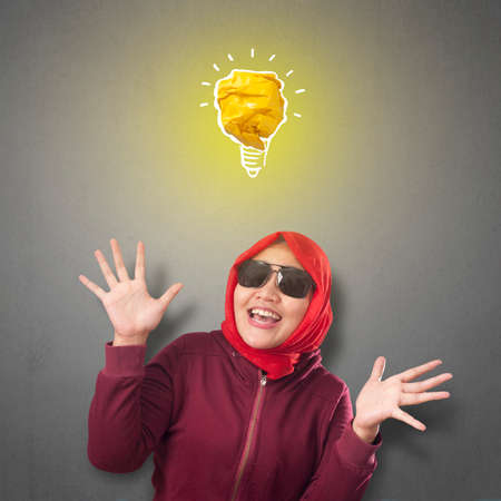 Portrait of successful beautiful Asian muslim woman smiling happy with bright light bulb lamp made of paper, symbol of idea creativity and innovationの写真素材