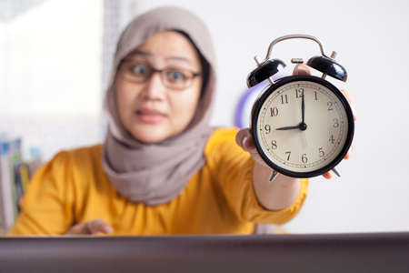 Young Asian businesswoman wearing suit and hijab worried by time when looking at a clock. Work deadline stress at the officeの写真素材