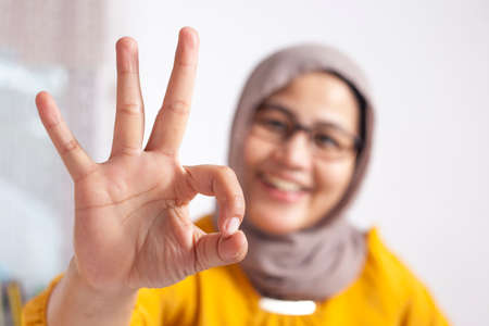Portrait of happy smiling Asian muslim woman shows OK fingersign gesture, businesswoman at the officeの写真素材