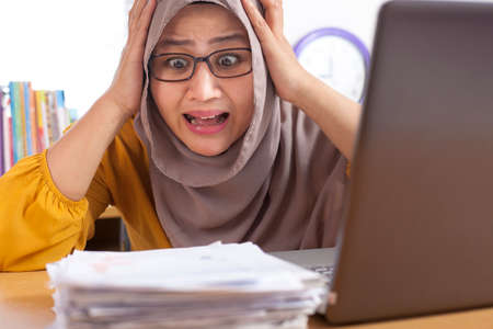 Portrait of Asian muslim businesswoman tired sick stress shocked headache gesture because of more paper work to do, overworked at the officeの写真素材