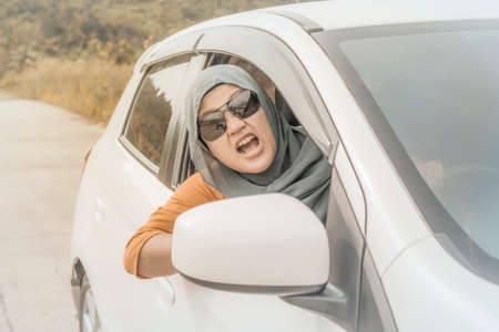 Portrait of Asian muslim lady driver getting mad and angry from the traffic, screaming and showing rude gesture from her carの写真素材