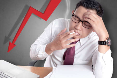 Portrait of Asian stressed Asian businessman smoking in his office, depression overworked failure conceptの写真素材