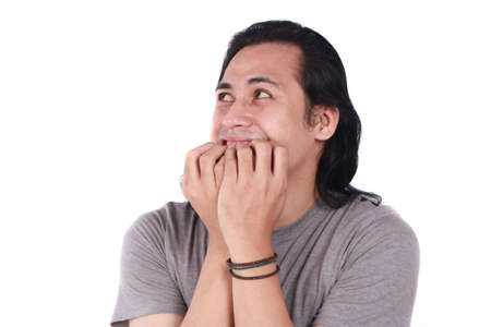 Portrait of young funny Asian man crying and  biting his nails as if he is worried afraid of...