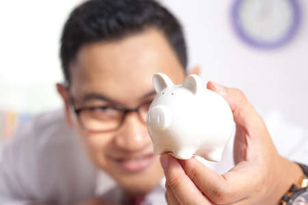 Portrait of happy successful Asian businessman holding piggy bank in hand, future investment conceptの写真素材