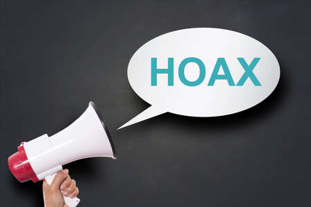 Hand holding megaphone agains blackboard with Hoax word in speech bubble concept