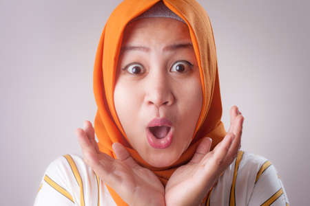 Portrait of cute young Asian muslim lady wearing hijab shows surprised or shocked expression with open mouth, close up facial expressionの写真素材