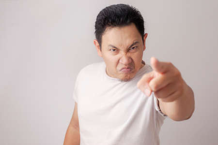 Photo image of funny Asian man showing cynical unhappy angry facial expression pointing forward giving warnの写真素材