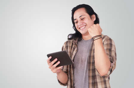 Portrait of a cute handsome young Asian man with long hair and funny face playing games on tablet