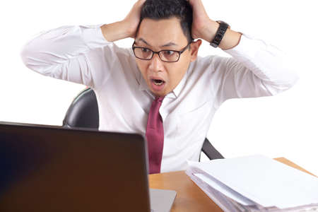Portrait of Asian businessman looking at his laptop with shocked stunned worried facial expression...