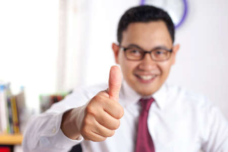 Portrait of young attractive Asian businessman working on laptop at the office, smiling happy...