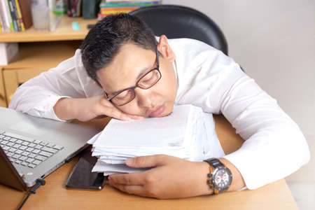 Portrait of Asian businessman tired for overworked and sleep in front of his laptop and paperworks...