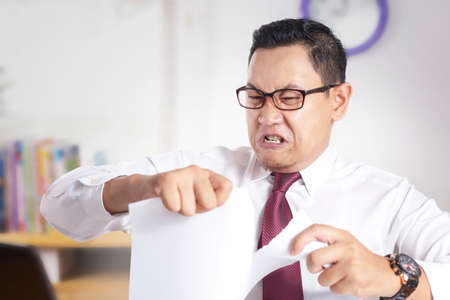 Portrait of angry mad young Asian businessman rip off contract paper, disappointed frustrated business workerの写真素材