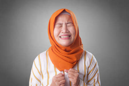 Portrait of sad Asian muslim woman crying against gray background