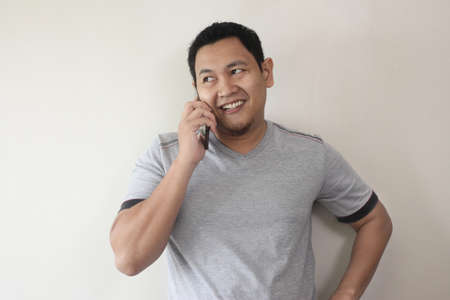 Attractive young Asian man talking on his phone, happy smiling laughing gesture