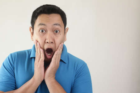Photo image of young funny Asian man shocked or surprised expression with mouth open, against white...