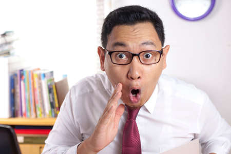 Portrait of funny Asian businessman shocked surprised with open mouth to see financial report, bad news conceptの写真素材