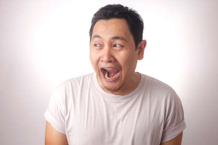 Portrait of funny young Asian man laughing smiling and looking to the side, over white backgroundの写真素材