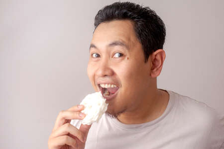 Portrait of funny good looking Asian young man eating kerupuk. Kerupuk is Indonesian fish or prawn cracker.の写真素材