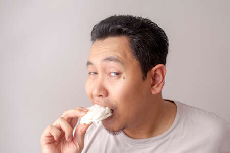 Portrait of funny good looking Asian young man eating kerupuk. Kerupuk is Indonesian fish or prawn...
