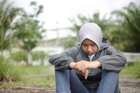Portrait of Asian muslim teenager girl stiing on the ground in the park, thinking gesture, depression conceptの写真素材