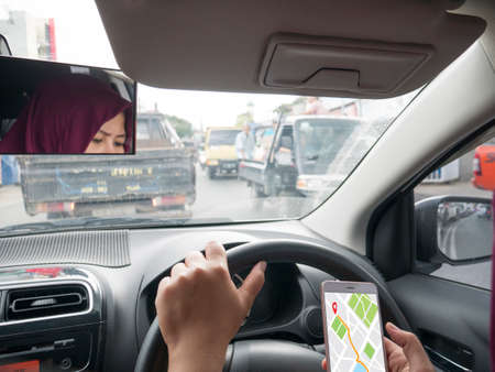 Car driver using smart phone with GPS map navigation while driving, car sharing app concept