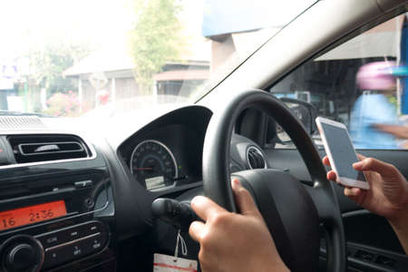 Close up image of a driver reading message on smart phone while driving a car, dangerous traffic...