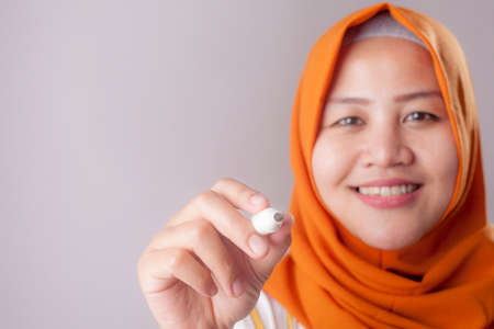 Portrait of young beautiful Asian muslim woman writing something in the air or virtual screen, smiling happy expressionの写真素材