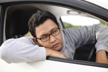 Portrait of funny Asian male driver get bored in his car trapped in traffic jam, tired lazy facial...