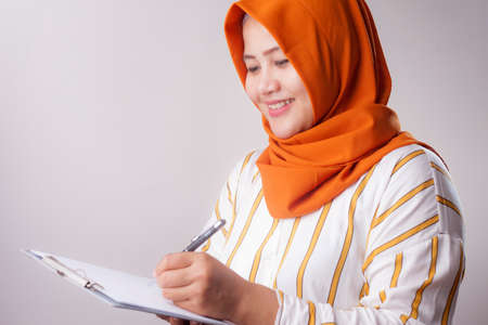 Portrait of beautiful young Asian muslim woman writing something, successful businesswoman checking recordsの写真素材
