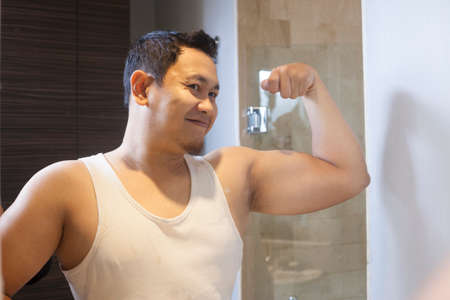 Portrait of funny attractive young narcissist Asian man smiling happily while looking at himself in...