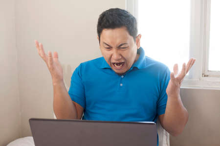 Portrait of young Asian man looked angry or diappointed looking at laptop, upset to see bad business...