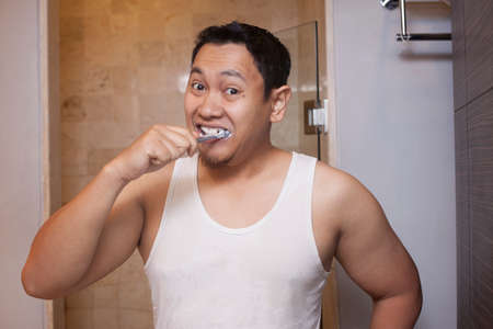Portrait of attractive young Asian male brushing his teeth in bathroomの写真素材
